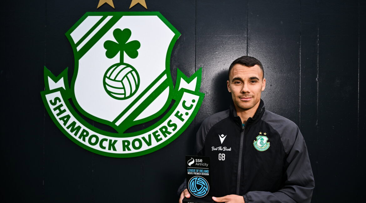 A man holding a soccer ball in front of a green and white logo.